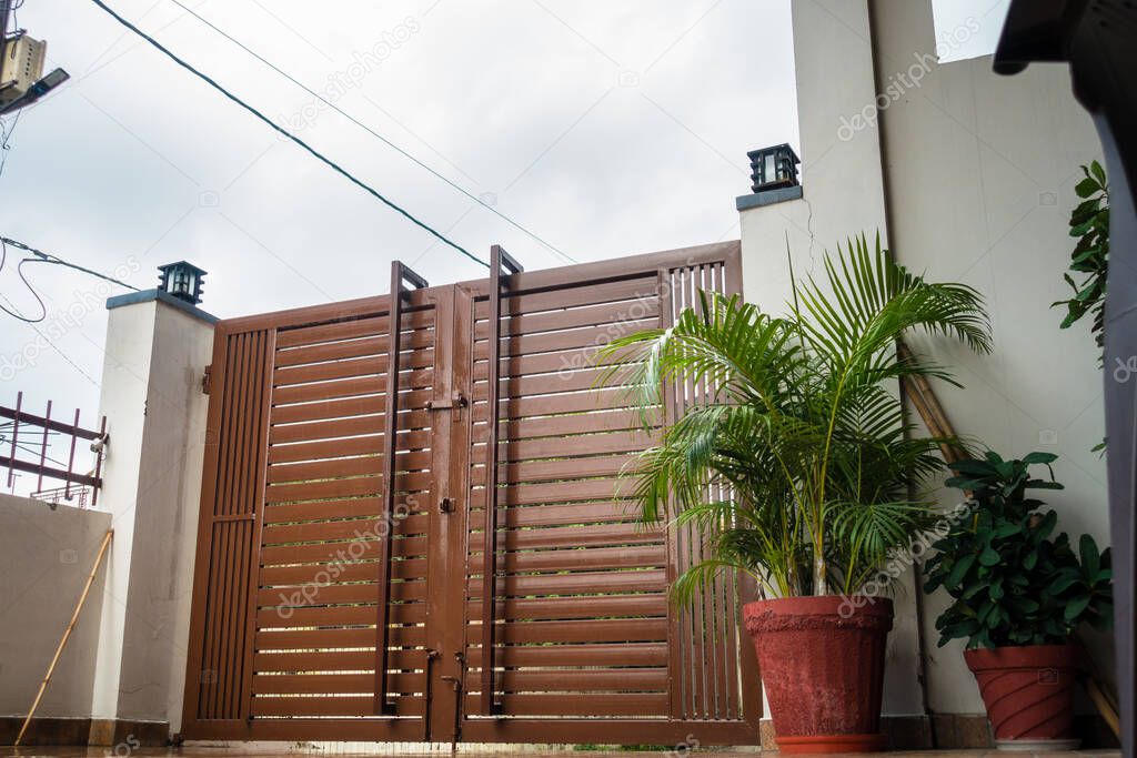 A large metal gate outside a residential home in India with flower pot in sides.