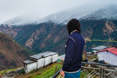 Uttarakhand. India. 23rd Jan2022.A Man standing on the roof of a village home with snow covered mountains of himalayas in the Okhimath district of Chamoli garhwal.