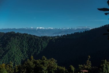A distant panoramic view of snow covered Gomukh glacier mountain peaks with forest cover in the upper Himalayas. Uttarakhand India.