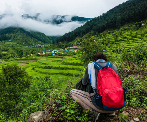 July 21st 2021. Uttarakhand India. A man with a red backpack taking a photograph of a village in the hills of the Himalayas.