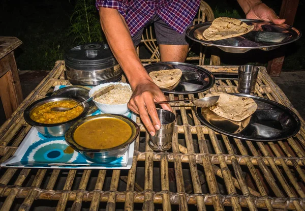 A man serving Indian meal of Rice, dal and chapati on a traditional bamboo table top.