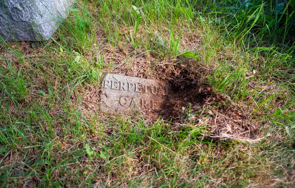 Antigua lápida cementerio medio enterrado lee cuidado perpetuo — Foto de Stock