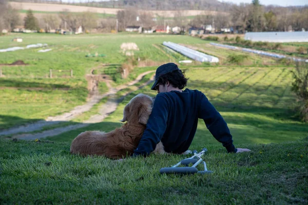 Jongeman knuffelt oude Golden Retriever op een heuvel met krukken op de grond — Stockfoto