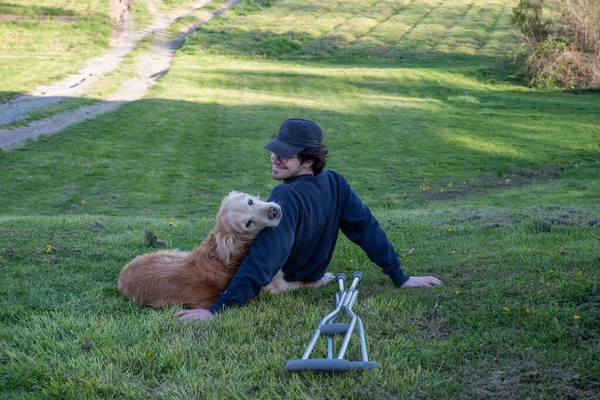 Velho cão Golden Retriever repousa em uma colina com um jovem com muletas — Fotografia de Stock