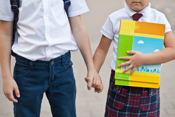 Niños colegial y colegiala en uniforme de pie cerca de la escuela y con las manos —  Fotos de Stock