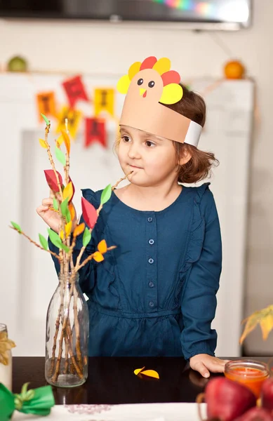戴着纸制火鸡帽的可爱小女孩在树枝上粘贴纸叶以庆祝感恩节。迪伊工艺艺术项目. — 图库照片