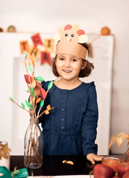 Little cute girl w papierowym kapeluszu indyka klei liście papieru na gałęziach do świętowania Święta Dziękczynienia. Projekt artystyczny Diy craft. — Zdjęcie stockowe