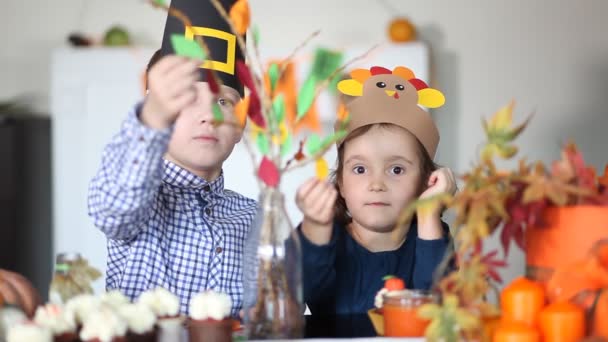Niño y niña linda en papel pavo y sombrero de peregrino pega hojas de papel en las ramas para celebrar el día de Acción de Gracias. Proyecto de arte artesanal Diy. — Vídeos de Stock