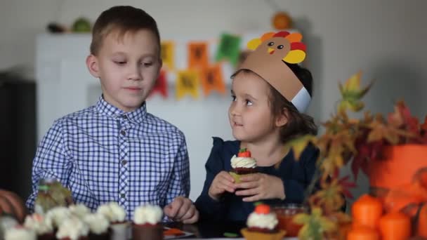 Ungarna sitter på festbordet och firar Thanksgiving-dagen. Barn i papper kalkon hatt och pilgrim hattar äta muffins och dricka mjölk. — Stockvideo