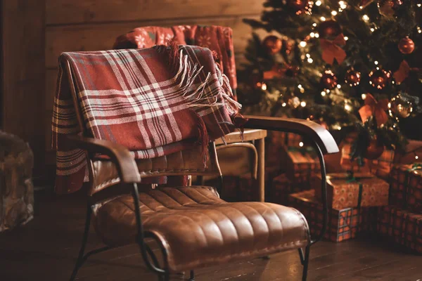 Interior decorated for Christmas. Armchair and Christmas tree on the background with lights.