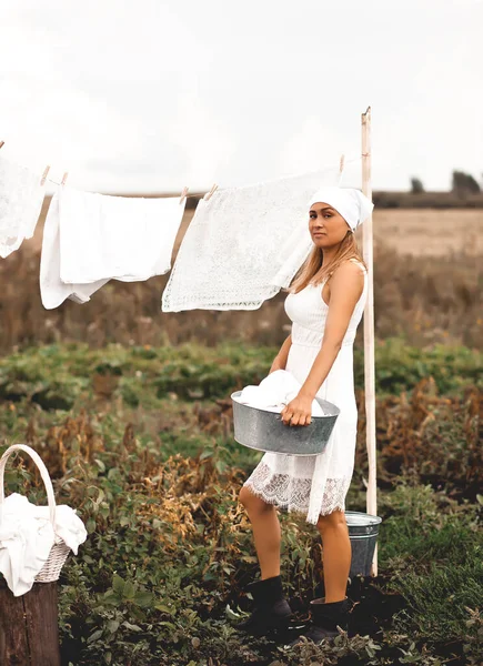 女性は晴れた日に洗濯室の屋外にぶら下がっている 女はバケツの水を持っている レトロなスタイル — ストック写真