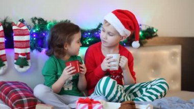 Noel Baba şapkalı ve Noel pijamalı çocuk kakao içiyor.