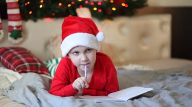 Noel Baba 'ya mektup yazan, Noel Baba şapkalı komik çocuk bir yatakta yatıyor.