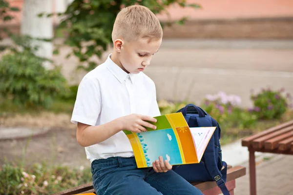 Školák v uniformě sedí na lavičce a čte si učebnici — Stock fotografie