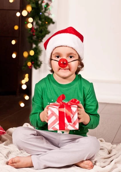 Happy little uśmiechnięta dziewczyna w Santa cap siedzi na kocu w piżamie Boże Narodzenie z pudełka prezentów. — Zdjęcie stockowe