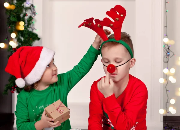 Happy little uśmiechnięta dziewczyna i chłopiec w czapce Santa i maska jelenia siedzi na kocu w piżamie Boże Narodzenie z pudełka prezentów. — Zdjęcie stockowe