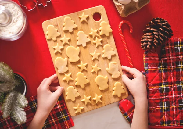 Selbst gebackene Weihnachtsplätzchen. Kinderhände halten ein Holzbrett mit rohen Plätzchen zum Backen bereit. Ansicht von oben — Stockfoto