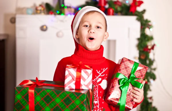 Chłopiec w dzianiny czerwony sweter i czapka Santa gospodarstwa Boże Narodzenie i Nowy Rok pudełka prezentów w domu. — Zdjęcie stockowe