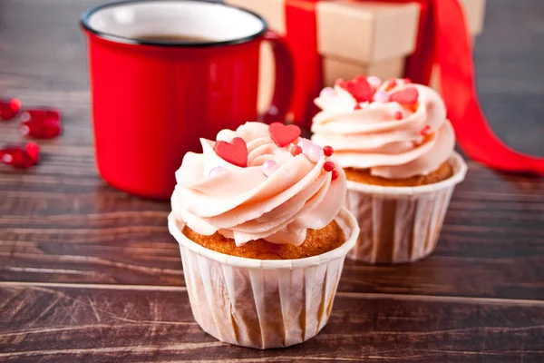 Cupcakes de San Valentín crema de queso glaseado decorado con caramelos del corazón, taza de café y caja de regalo en el fondo de madera. —  Fotos de Stock