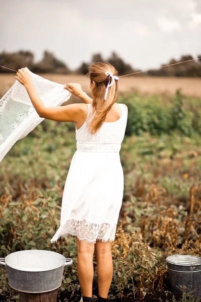 Jovem mulher em um vestido branco pendurado lavanderia ao ar livre — Fotografia de Stock