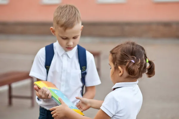 Kid uczennica dać uczennicy w mundurowych podręczników szkolnych — Zdjęcie stockowe