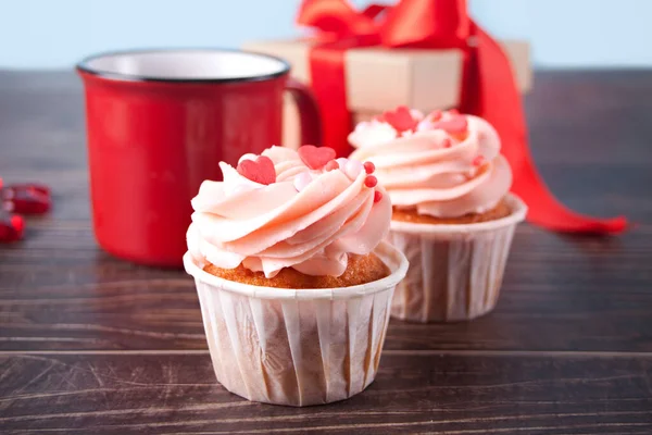 Cupcakes de San Valentín crema de queso glaseado decorado con caramelos del corazón, taza de café y caja de regalo en el fondo de madera. — Foto de Stock