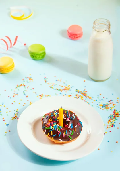 Delicioso donut com cobertura de chocolate e vela de aniversário com garrafa de leite e macaroons no fundo. — Fotografia de Stock