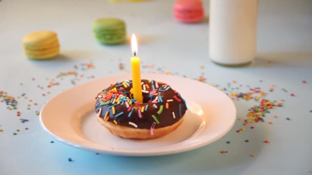 Νόστιμο ντόνατ με γλάσο σοκολάτας και κερί γενεθλίων με μπουκάλι γάλα και αμυγδαλωτά στο παρασκήνιο. Κάποιος σβήνει τα κεριά.. — Αρχείο Βίντεο