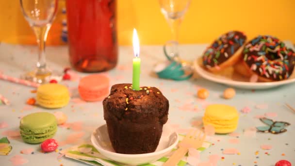Heerlijke chocolade muffin cupcake met verjaardagskaars en andere zoetigheden en snoepjes op de achtergrond. Partijconcept — Stockvideo