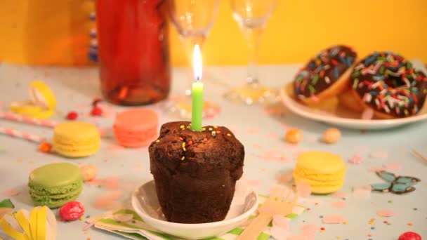 Heerlijke chocolade muffin cupcake met verjaardagskaars en andere zoetigheden en snoepjes op de achtergrond. Partijconcept — Stockvideo