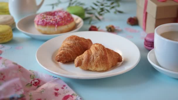 Woman hand take one fresh baked croissant. Cup of tea and donut on the background. Healthy lifestyle concept — Stock Video