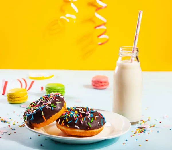 Delicioso donut com cobertura de chocolate e vela de aniversário com garrafa de leite e macaroons no fundo. — Fotografia de Stock