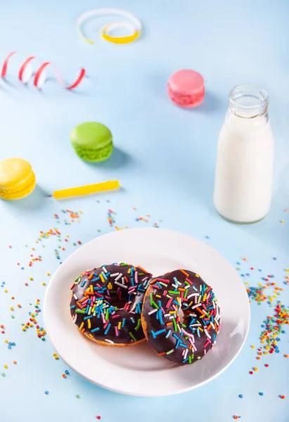 Deliciosos donuts com cobertura de chocolate e vela de aniversário com garrafa de leite e macaroons no fundo. — Fotografia de Stock