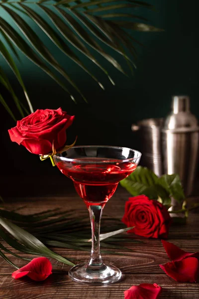 Köstliche Erfrischungsgetränke trinken roten Cocktail mit roten Rosen und Blütenblättern auf einem Holztisch. Romantisches Konzept zum Valentinstag. lizenzfreie Stockbilder