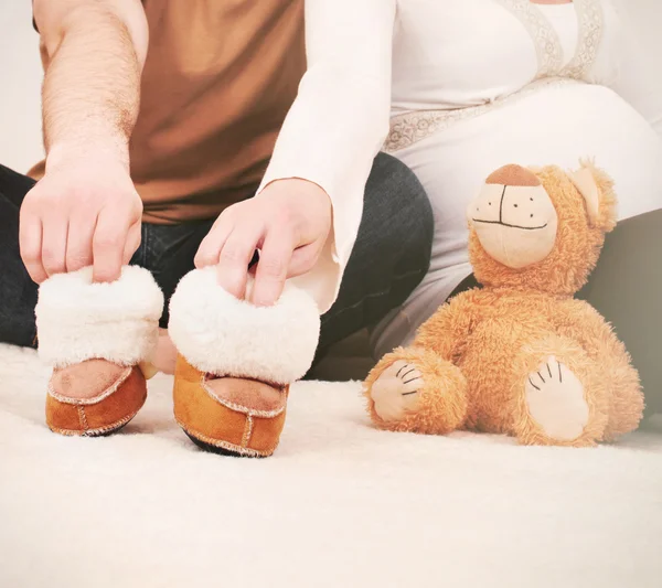 Manos de pareja embarazada con pequeñas botas para bebé — Foto de Stock