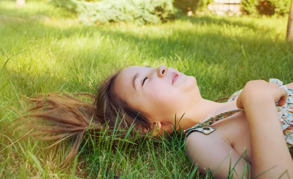 Boldog, mosolygós kislány feküdt a füvön, napsütéses nyári napon — Stock Fotó