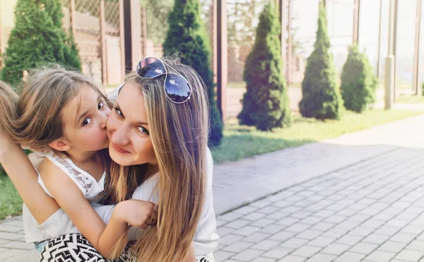 Little cute girl kissing her beautiful mum outdoor in the park — Stock Photo, Image