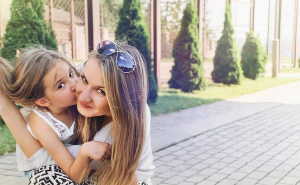 Kleines süßes Mädchen küsst ihre schöne Mutter im Freien im Park — Stockfoto