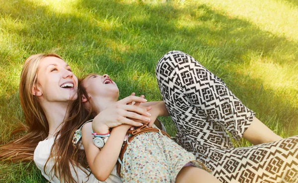 Счастливая маленькая девочка и ее мать веселятся на траве под солнцем — стоковое фото