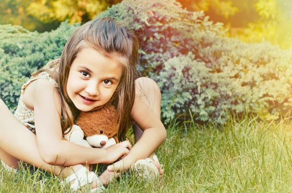 Roztomilý úsměvem holčička hospodářství medvídek a sedí na g — Stock fotografie