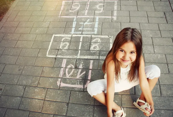 Красивая веселая маленькая девочка играет в классики на детской площадке — стоковое фото
