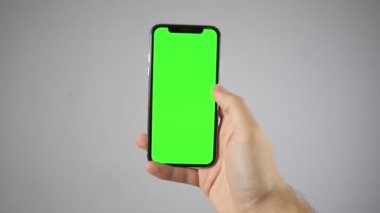 Elinde bir iPhone tutuyor. Telefondaki yeşil ekran. Bir iPhone 'un maketi. Elde elma ürünü. Telefonun dikey ve yatay eğimi.