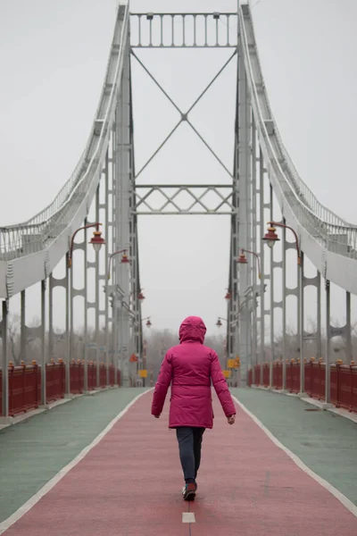 A woman walks across a bridge. Photographed on a pedestrian bridge in Kyiv, Ukraine. A woman on a bridge. Woman in jacket.