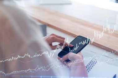 Elinde akıllı bir telefon tutan ve doğru yatırım çözümlerine ulaşmak için borsayı araştıran bir kadın tüccar. İnternet ticareti ve zenginlik yönetimi kavramı. Hologram Forex çizelgesi.