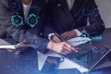 İki bilişim teknolojisi uzmanı iş hizmetlerini geliştirmek için yazılım geliştirmek üzere yeni bir yaklaşım geliştirme projesi üzerinde çalışıyor. Masanın üzerinde belgeyle birlikte teknolojik simgeler.