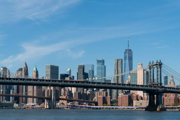 Brooklyn and Manhattan bridges with New York City financial downtown skyline panorama at day time over East River with blue cloudy sky.