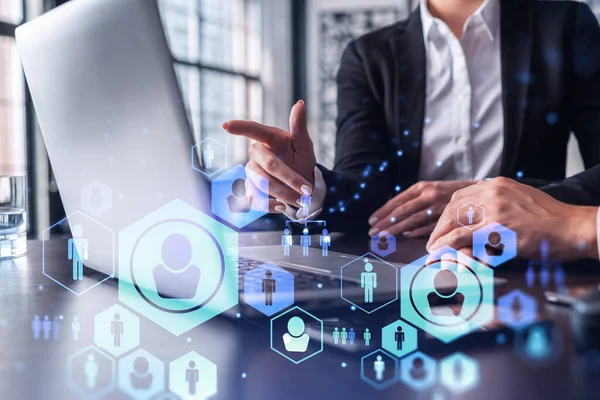 Two HR specialists analyzing the recruitment market using laptop to boost the intern program at international consulting company. Social networking hologram icons. — Stock Photo, Image