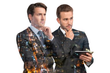 Takım elbiseli iki yakışıklı iş adamı, tablet aleti kullanıyorlar ve düşünceli davranıyorlar. Asya kurumsal yaşam tarzı, çeşitli genç profesyonellerin iletişimi. Gece Bangkok şehri manzarası. Çift pozlama