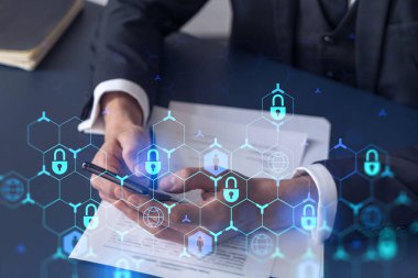 Resmi görevli bir işadamı siber güvenlikte risk olasılığını önlemek ve telefonda detayları kontrol etmek için sözleşmeyi okuyor. Çalışma masasının üzerine asma kilit hologramı simgeleri.