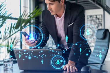 Takım elbiseli iş adamı uluslararası iş danışmanlığı için yeni adayları kontrol etmek için akıllı telefon kullanıyor. HR ve sosyal medya simgeleri modern panoramik ofis geçmişi üzerine.